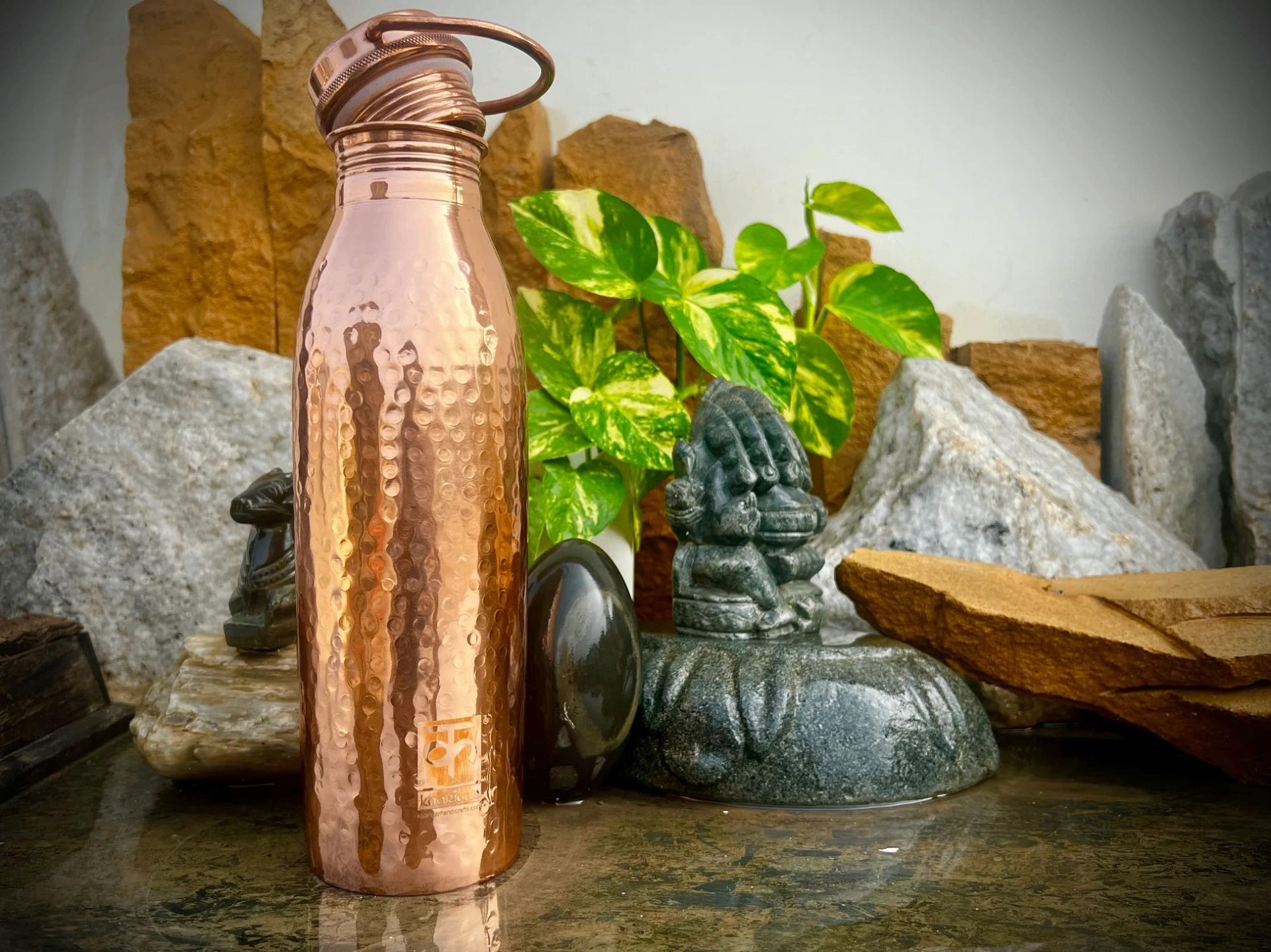 Hammered pure copper water bottle resting on stone with greenery
